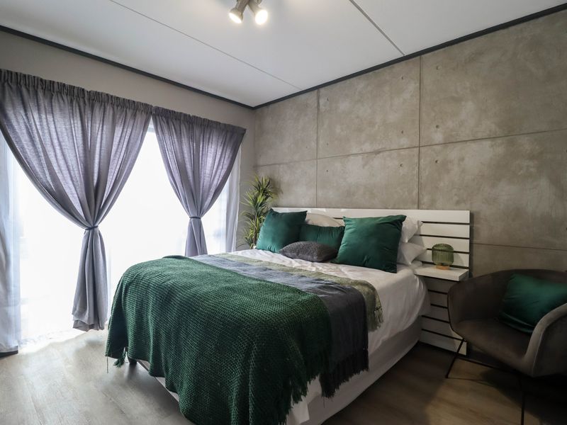 A modern bedroom featuring a concrete panel feature wall, laminate flooring, and large windows with curtains.