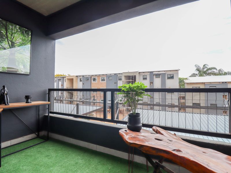 A covered balcony featuring a metal balustrade and artificial grass flooring, offering an outdoor space with views of the surrounding complex.