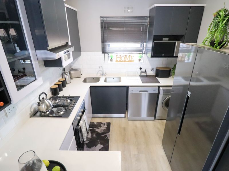 Modern kitchen featuring dark cabinetry, white countertops, subway tile backsplash, gas hob, built-in oven, and integrated space for appliances.