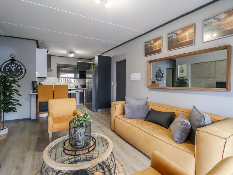 A well-maintained open-plan living and kitchen area featuring modern laminate flooring, neutral wall tones, and a functional breakfast bar layout.