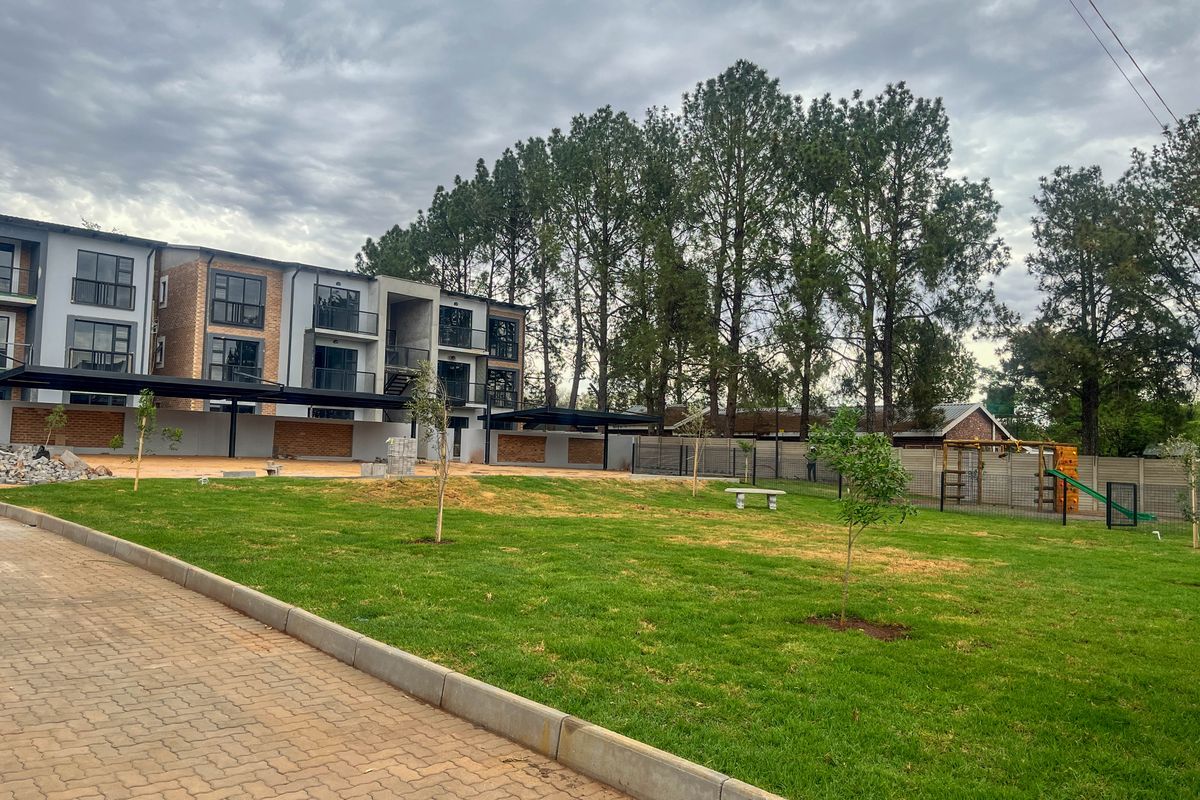 View of the rear exterior of the townhouse complex, featuring a paved driveway, landscaped lawn, and covered carport structures.