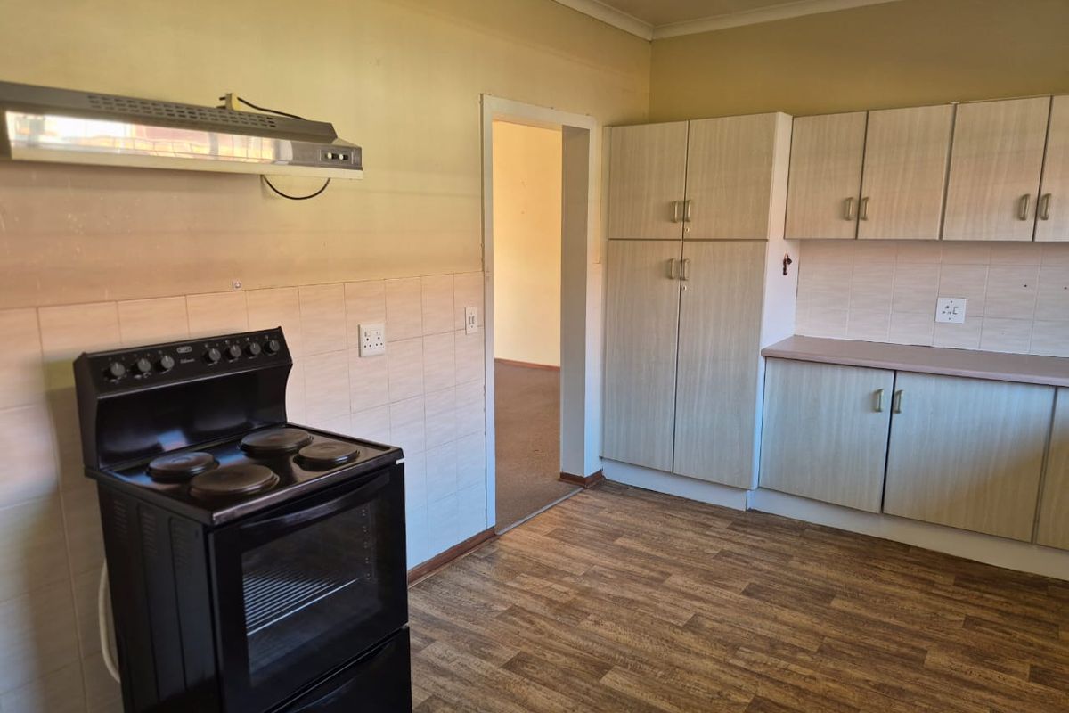 A functional kitchen featuring wood-look laminate flooring, built-in cabinetry, a freestanding electric stove, and an extractor fan.