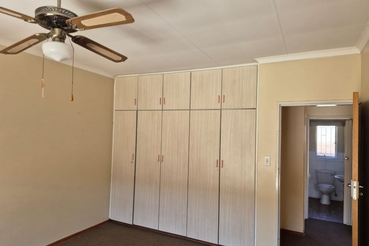 A bedroom featuring built-in wooden cupboards, a ceiling fan, and direct access to an en-suite bathroom.