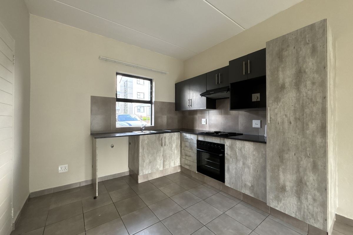 A clean, modern kitchen featuring built-in cabinetry, a hob, oven, extractor fan, and tiled finishes, presented in an empty, move-in ready condition.