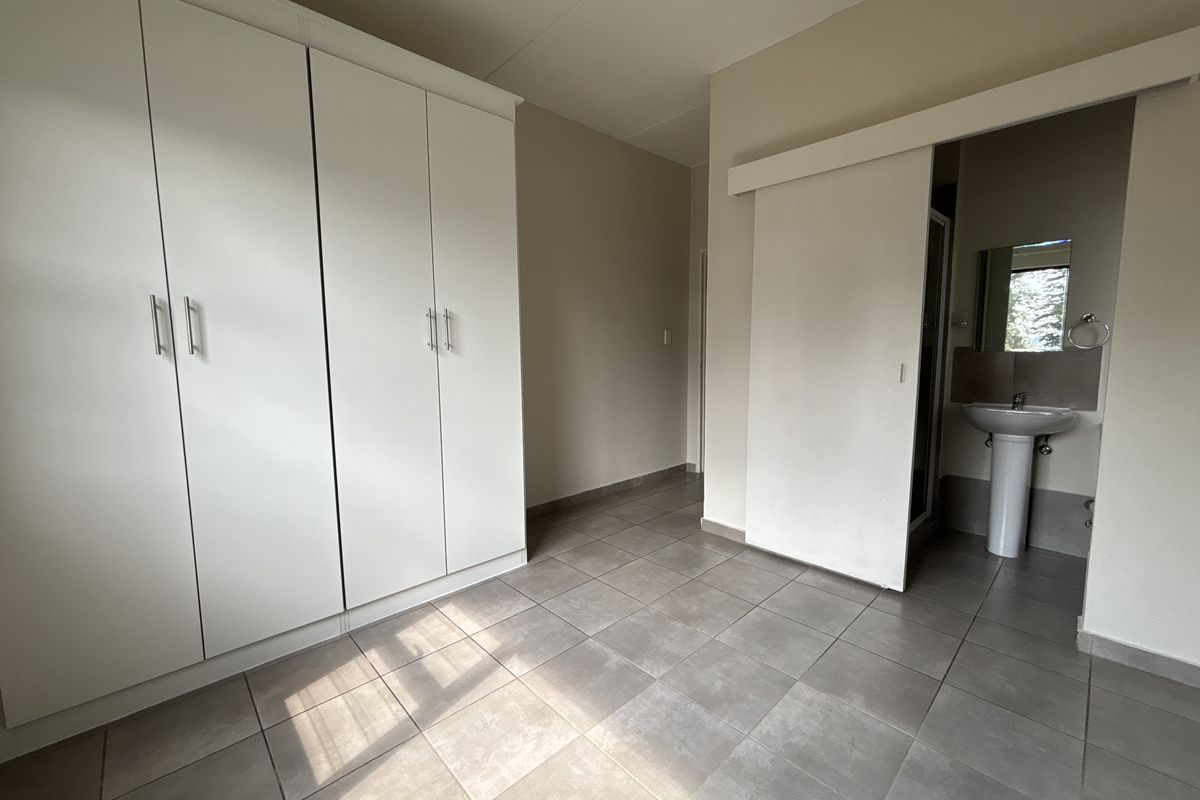 A clean, empty bedroom featuring built-in cupboards, tiled flooring, and an en-suite bathroom area with a pedestal basin.