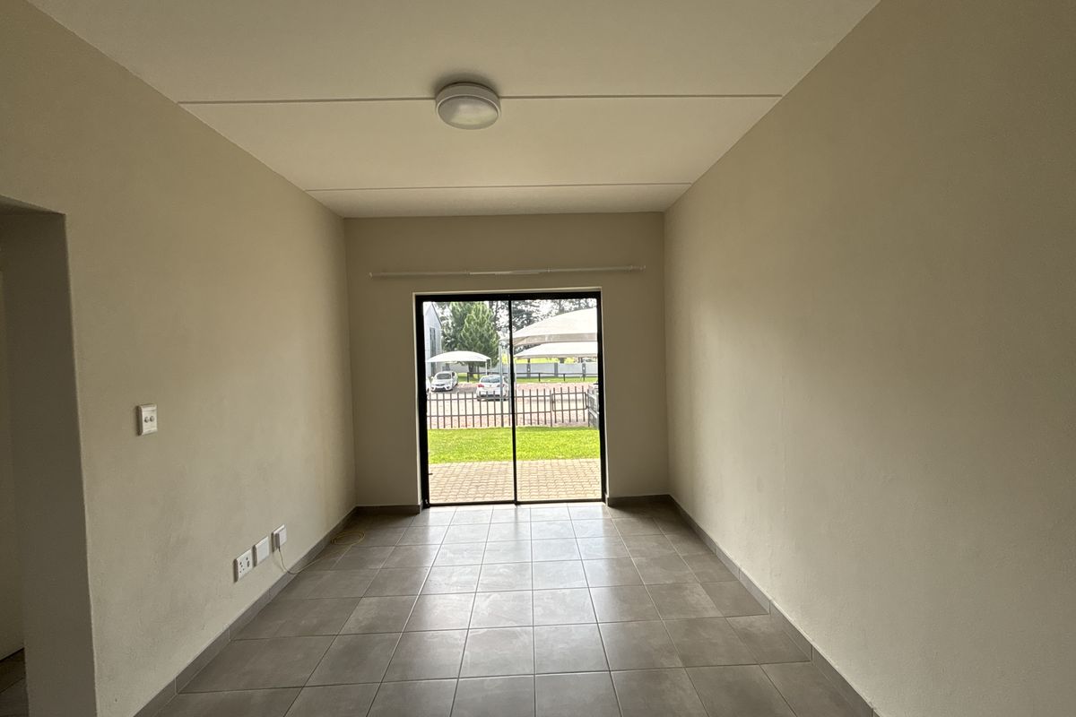 An empty, neutral-toned living room featuring tiled flooring and a sliding glass door that provides access to the exterior area.