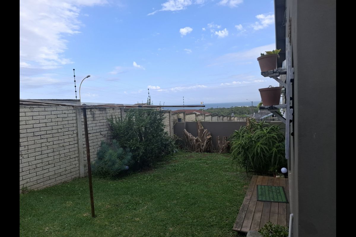 A private rear garden featuring a lawn area, perimeter brick boundary walls with electric fencing, and a small wooden deck section.