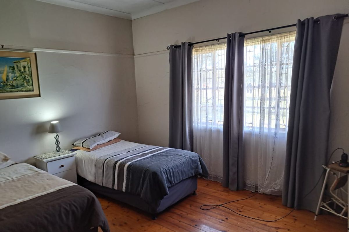 A bedroom featuring original timber flooring, large windows with security bars, and high ceilings with a picture rail.