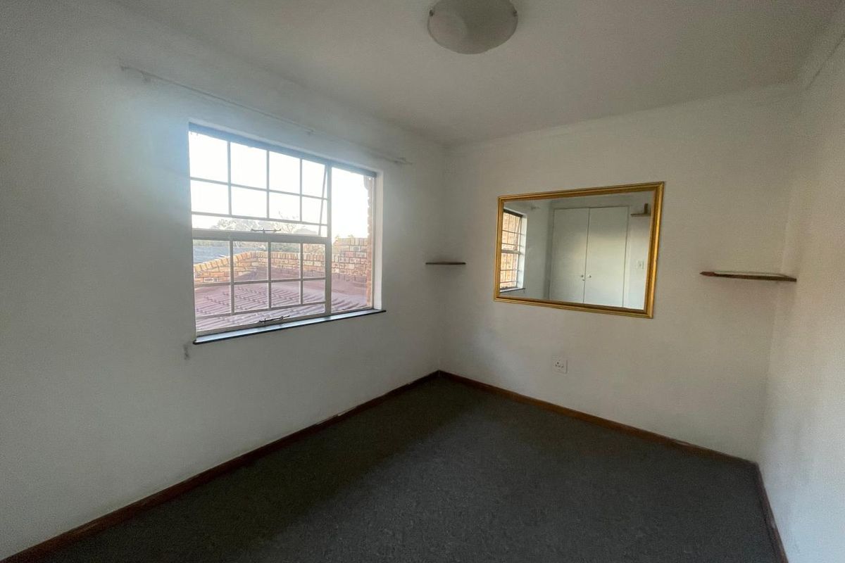 A simple, empty bedroom featuring carpeted flooring, a built-in cupboard, and a window with natural light.