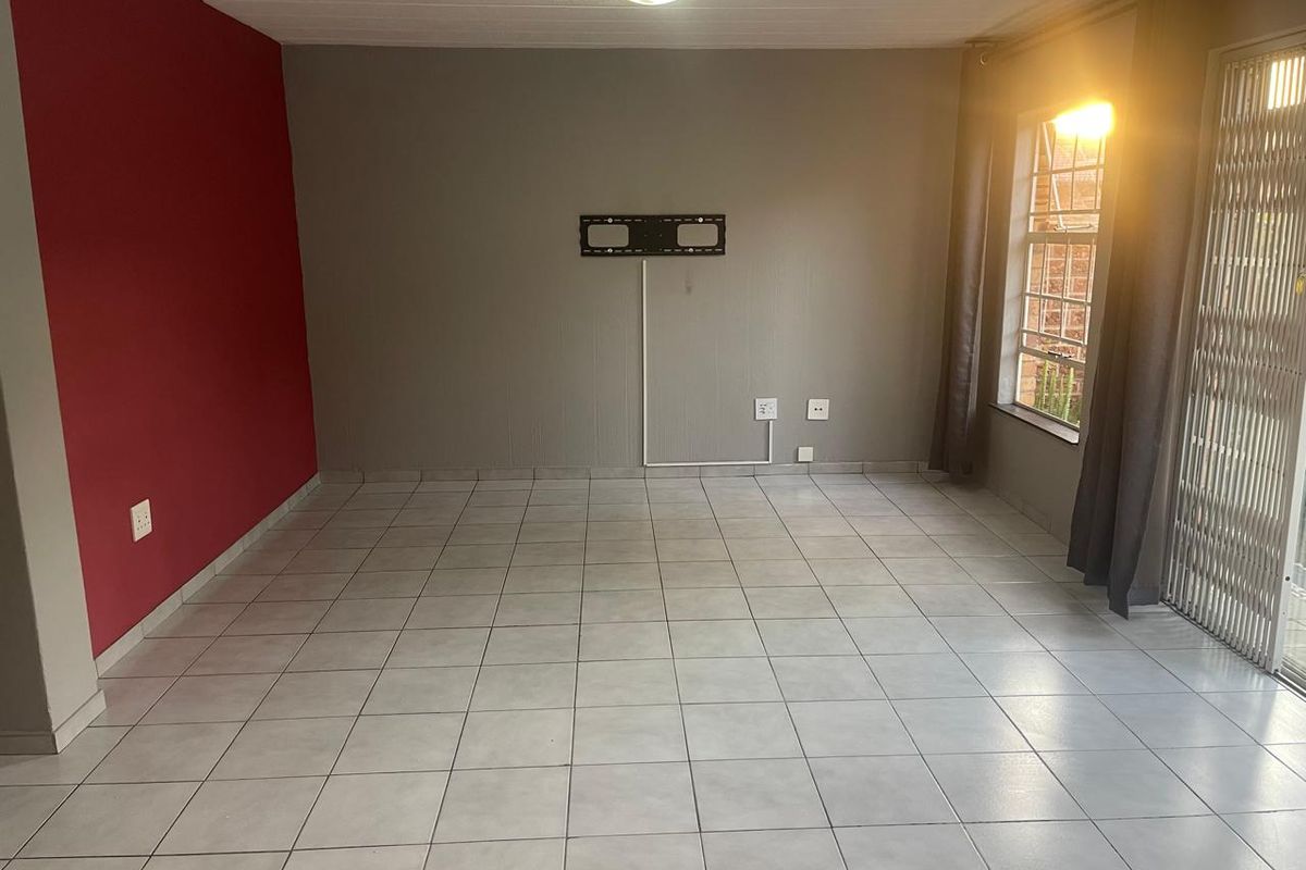 An empty living room featuring tiled flooring, a wall-mounted TV bracket, and access to an outdoor area through a security gate.