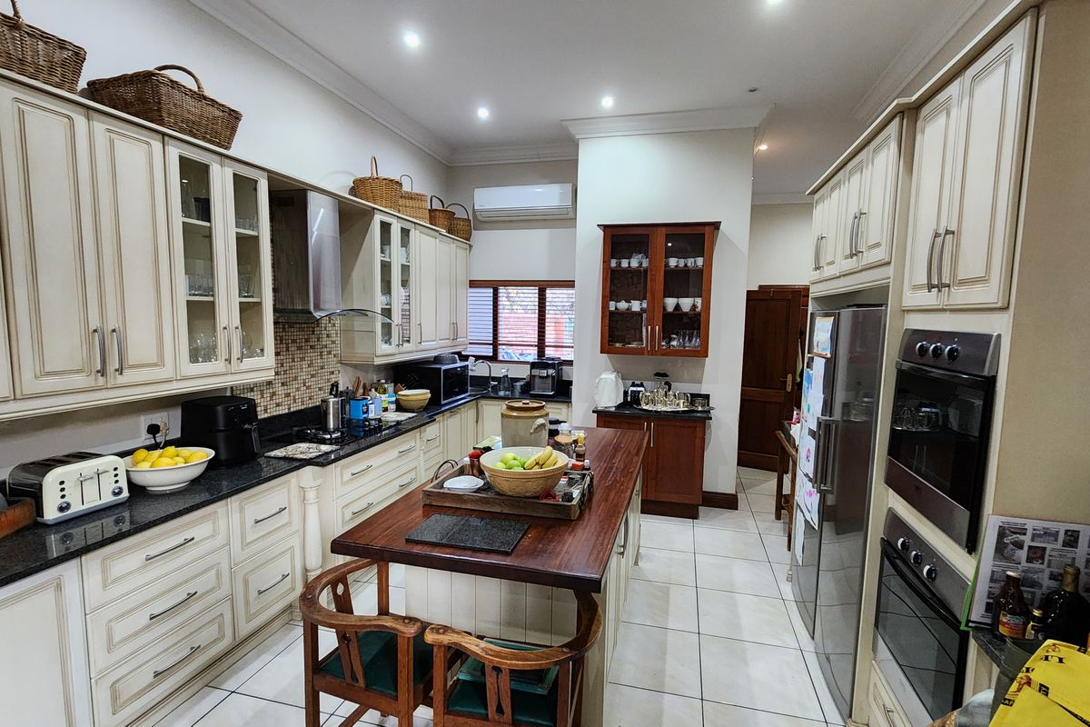 Spacious kitchen featuring classic cream cabinetry, granite countertops, a central wooden island, built-in appliances, and tiled flooring with recessed lighting.