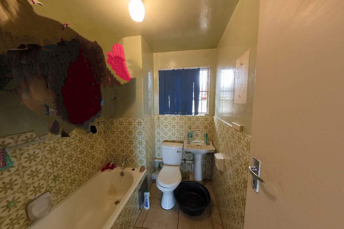 A dated bathroom featuring a bathtub, pedestal basin, and toilet with vintage patterned wall tiles and visible wall surface deterioration.
