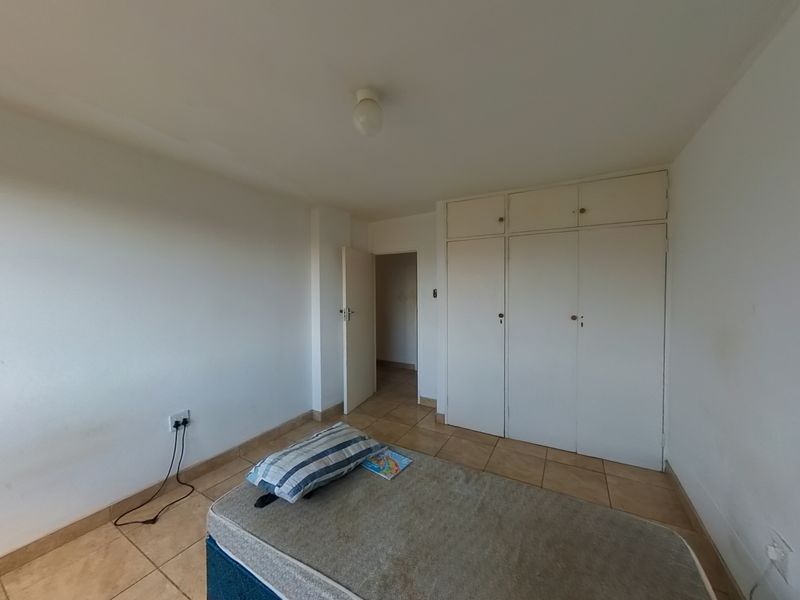 A functional bedroom featuring tiled flooring and built-in cupboards, offering a neutral space ready for personalization.