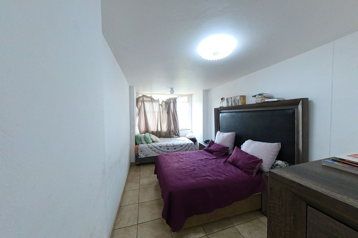 A bedroom featuring tiled flooring and a central ceiling light, showing signs of wear on the walls.