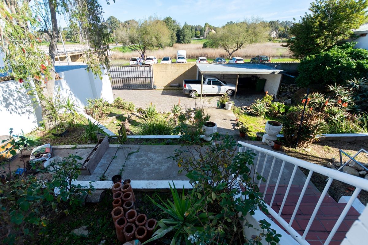 Rear exterior view featuring a paved driveway, carport, and tiered garden area with concrete stairs and metal railings.