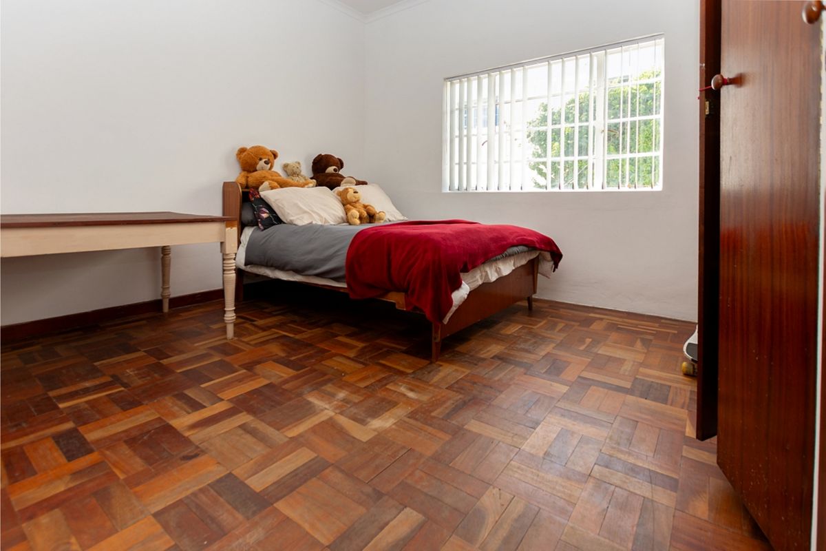 A bedroom featuring classic parquet flooring, a window with vertical blinds, and a solid timber door, offering a functional space with original character.