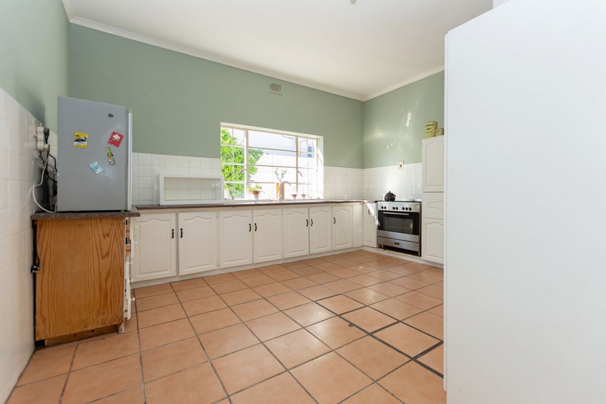 A functional kitchen featuring white cabinetry, tiled splashbacks, and tiled flooring, offering a classic layout with potential for modern updates.