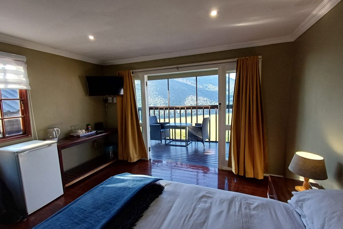 A comfortable bedroom featuring timber flooring, recessed lighting, and a sliding glass door that opens onto a private balcony with scenic mountain views.