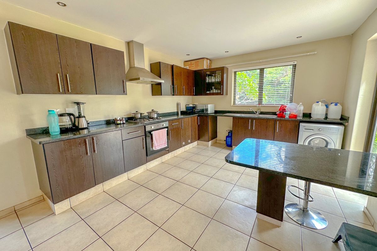 A functional kitchen featuring dark wood cabinetry, granite countertops, a built-in oven, extractor fan, and tiled flooring with an integrated breakfast bar.