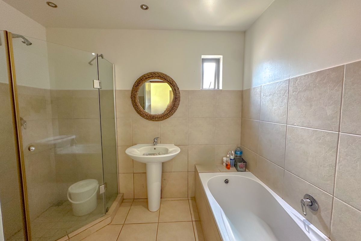 A functional bathroom featuring a pedestal basin, a built-in bathtub, and a separate glass-enclosed shower with neutral wall and floor tiling.
