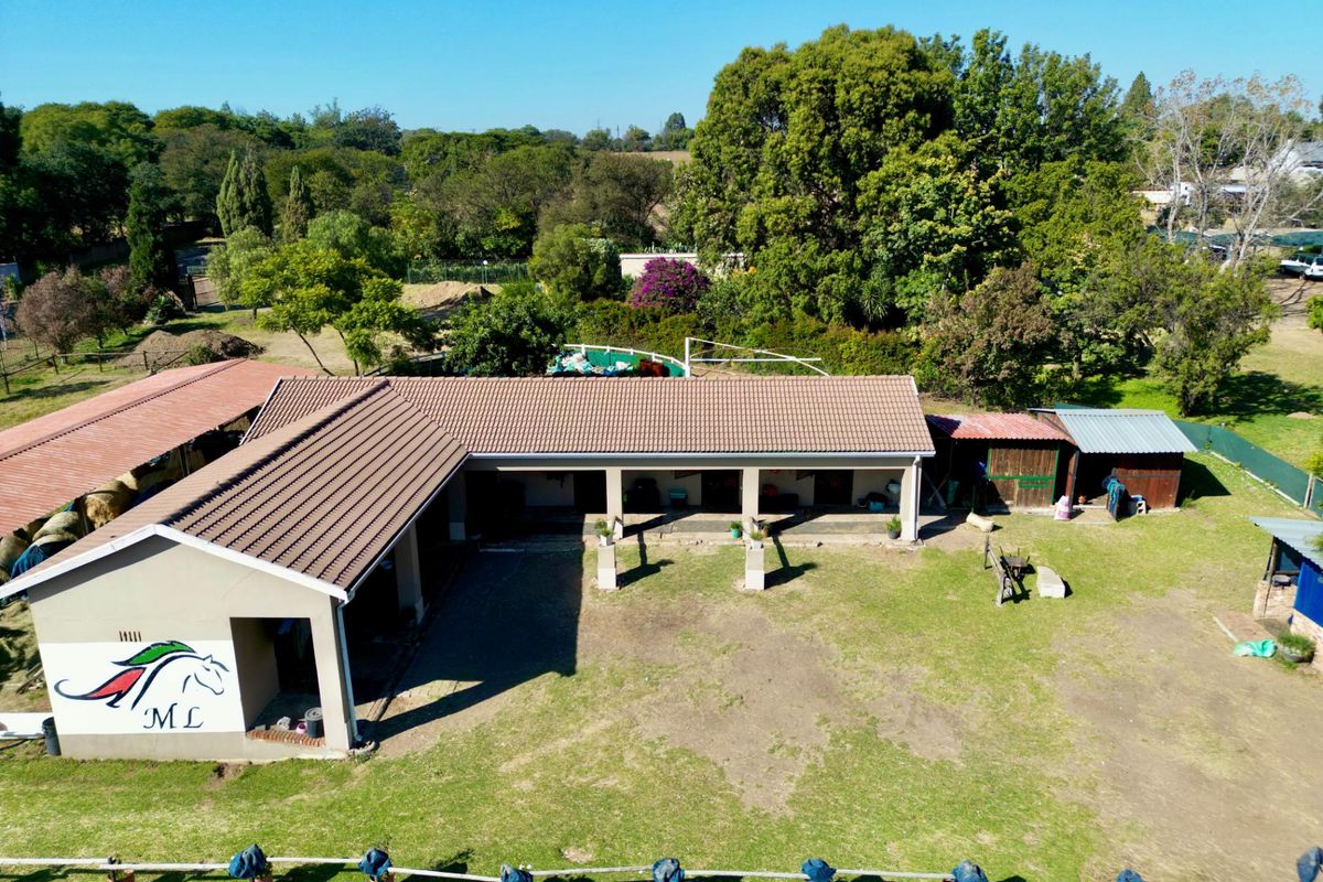 Aerial view of a stable or equestrian facility featuring a tiled roof structure, open-sided bays, and surrounding landscaped grounds.