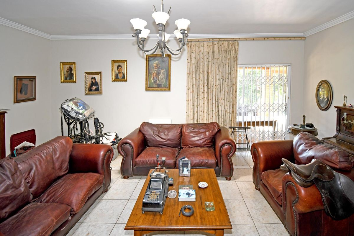 A spacious living room featuring tiled flooring, a central chandelier, and sliding glass doors with security gates leading to the outdoor area.