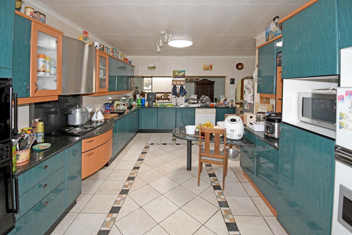 Spacious kitchen featuring extensive teal and wood-tone cabinetry, granite countertops, integrated oven, and a central breakfast bar area with tiled flooring.