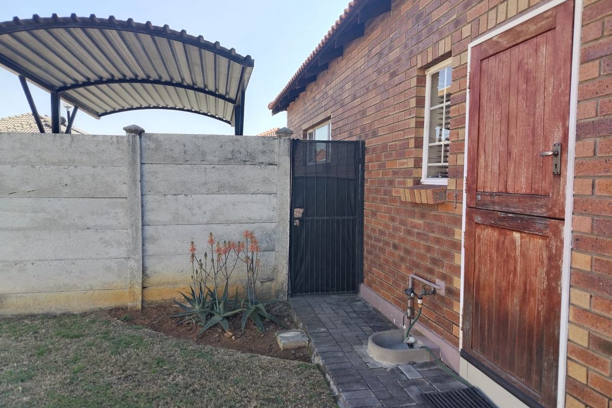 Rear exterior view featuring a face brick facade, paved walkway, metal security gate, and a covered carport structure.