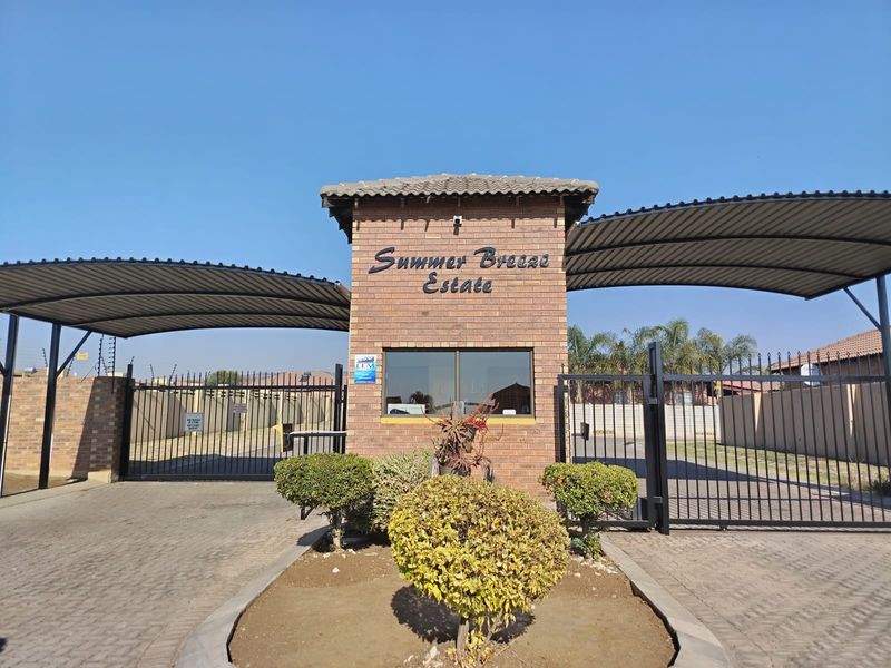 The main entrance gate and guardhouse of Summer Breeze Estate, featuring brick construction, metal security gates, and paved driveway access.