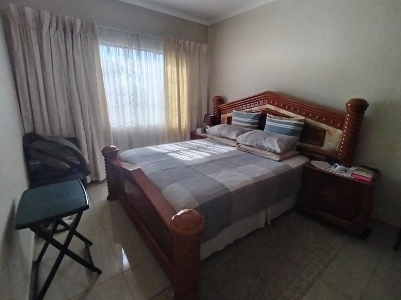 A standard bedroom featuring tiled flooring and large windows with curtain rails, offering a functional space with neutral wall finishes.