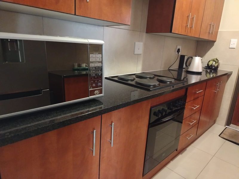 A functional kitchen featuring wooden cabinetry, granite countertops, a built-in oven, and an electric hob with tiled flooring.