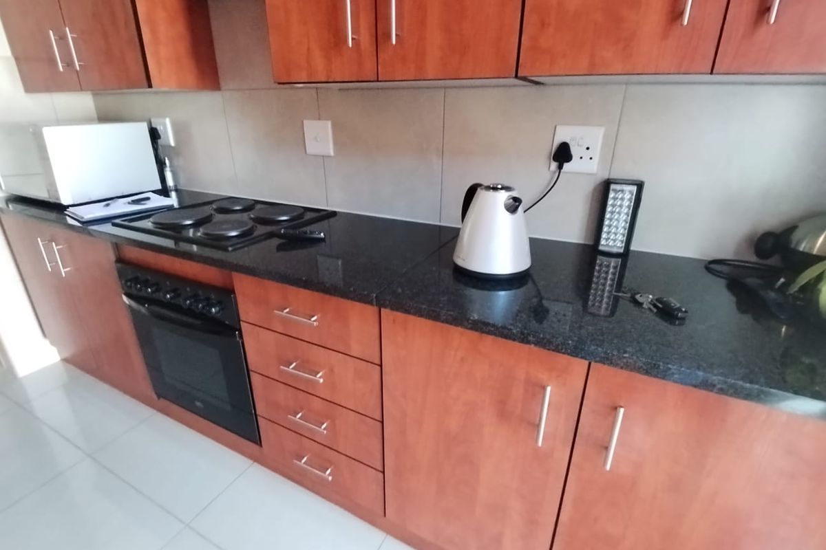 A functional kitchen featuring dark granite countertops, wood-finish cabinetry, and a built-in electric oven and hob with tiled splashbacks.