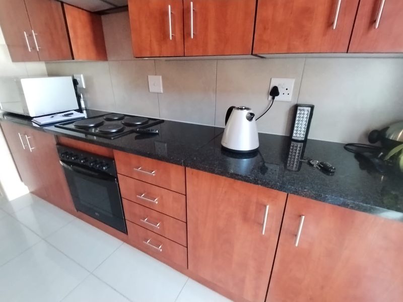 A functional kitchen featuring dark granite countertops, wood-finish cabinetry, and a built-in electric oven and hob with tiled splashbacks.