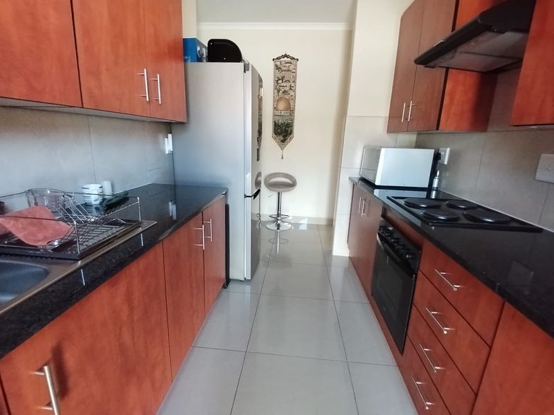 A functional galley-style kitchen featuring granite countertops, dark wood-finish cabinetry, built-in oven, electric hob, and tiled flooring.