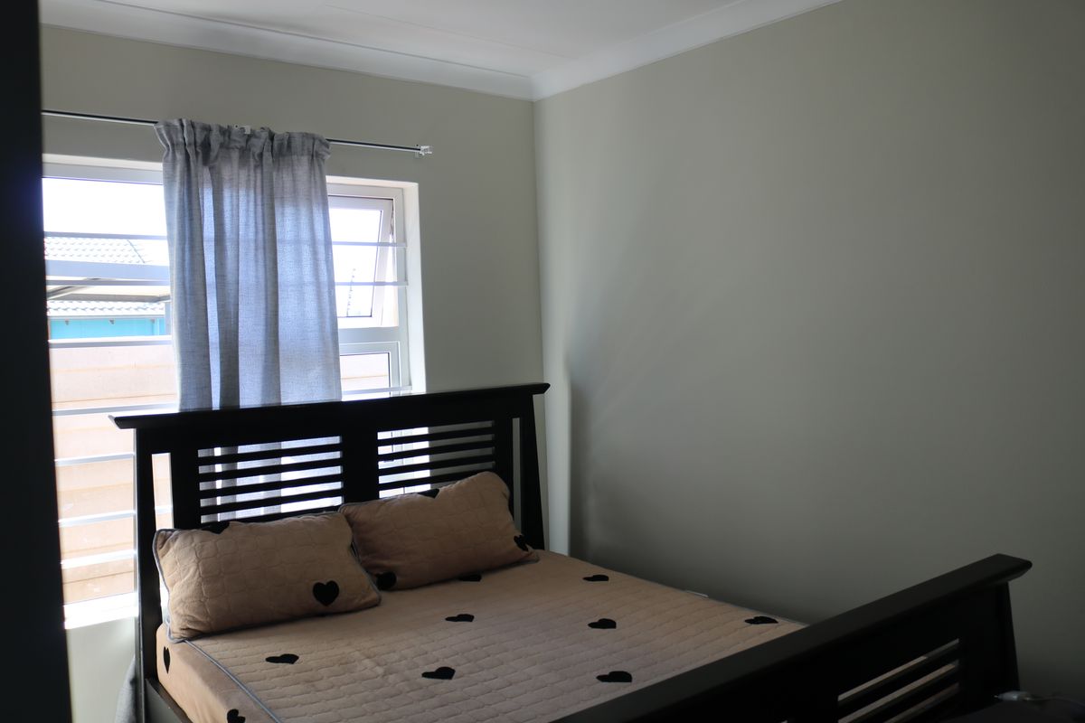 A standard bedroom featuring neutral wall paint, a window with security bars, and crown molding.