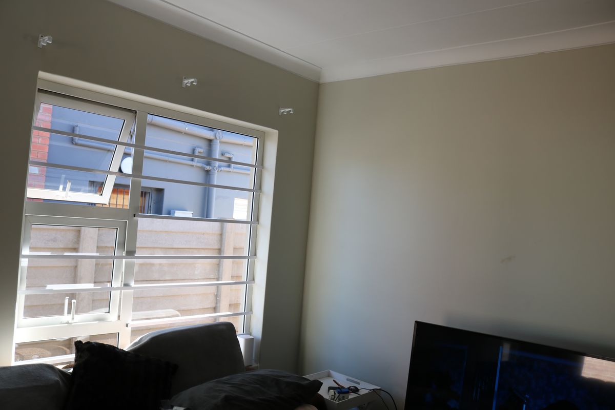 A living room area featuring neutral wall tones, aluminium window frames with security bars, and decorative cove cornicing.