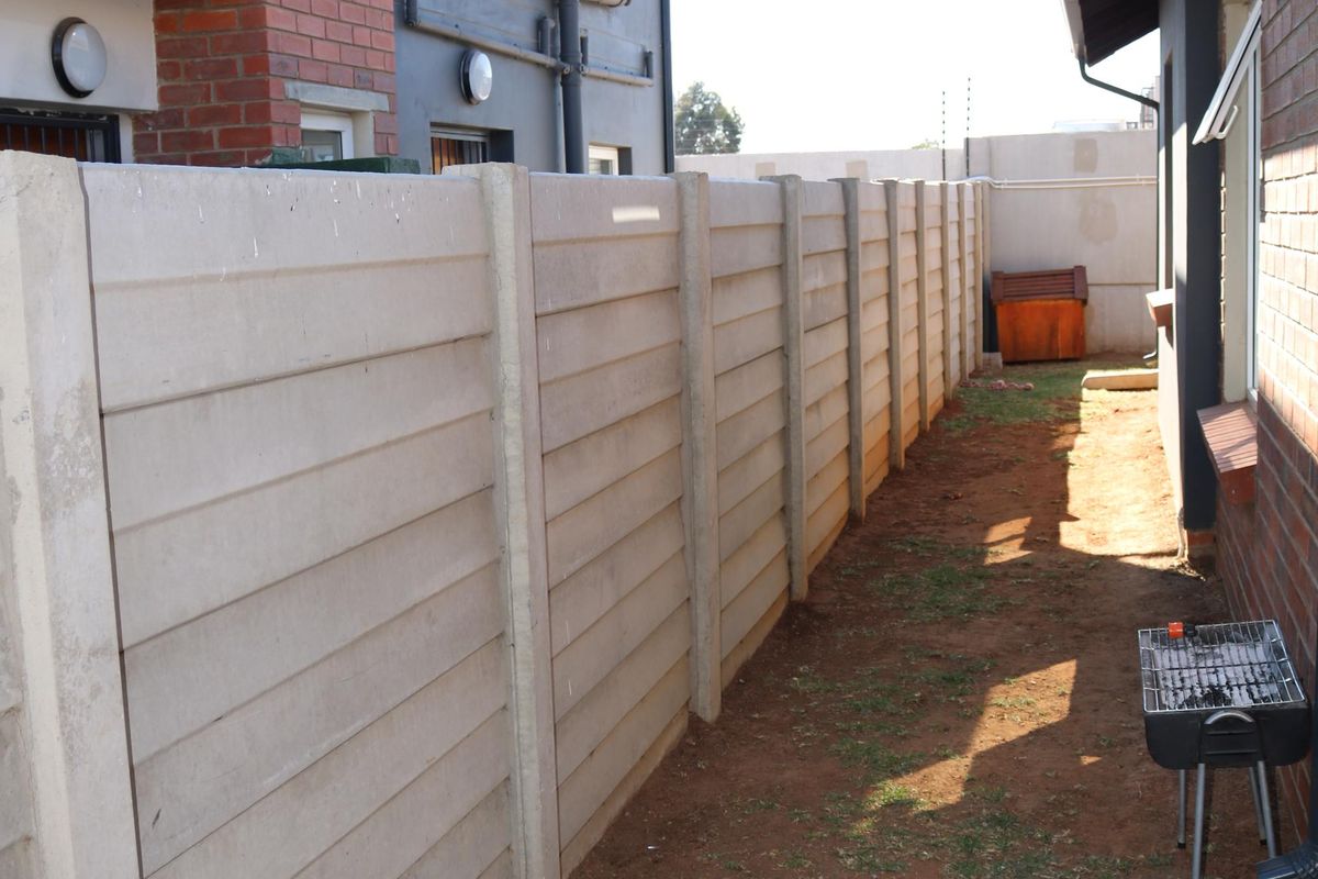 A side yard area featuring a precast concrete boundary wall, brick paving, and access to the rear of the residential building.