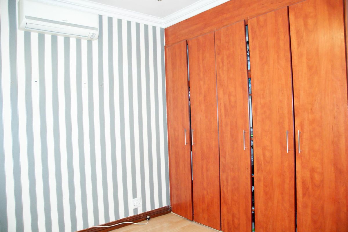 Bedroom featuring built-in wooden cabinetry, striped wallpaper, and a wall-mounted air conditioning unit.