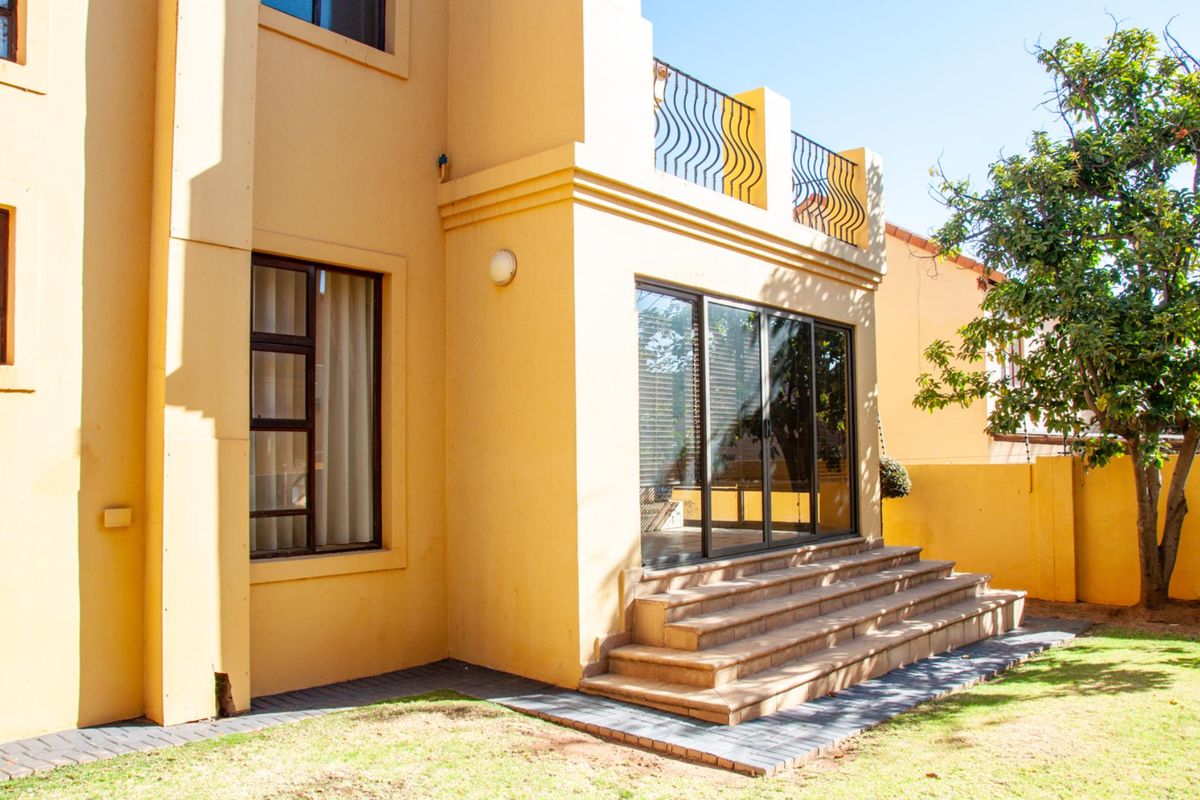 Rear view of the property featuring a paved patio area, tiled steps leading to sliding glass doors, and a balcony with decorative metal railings.