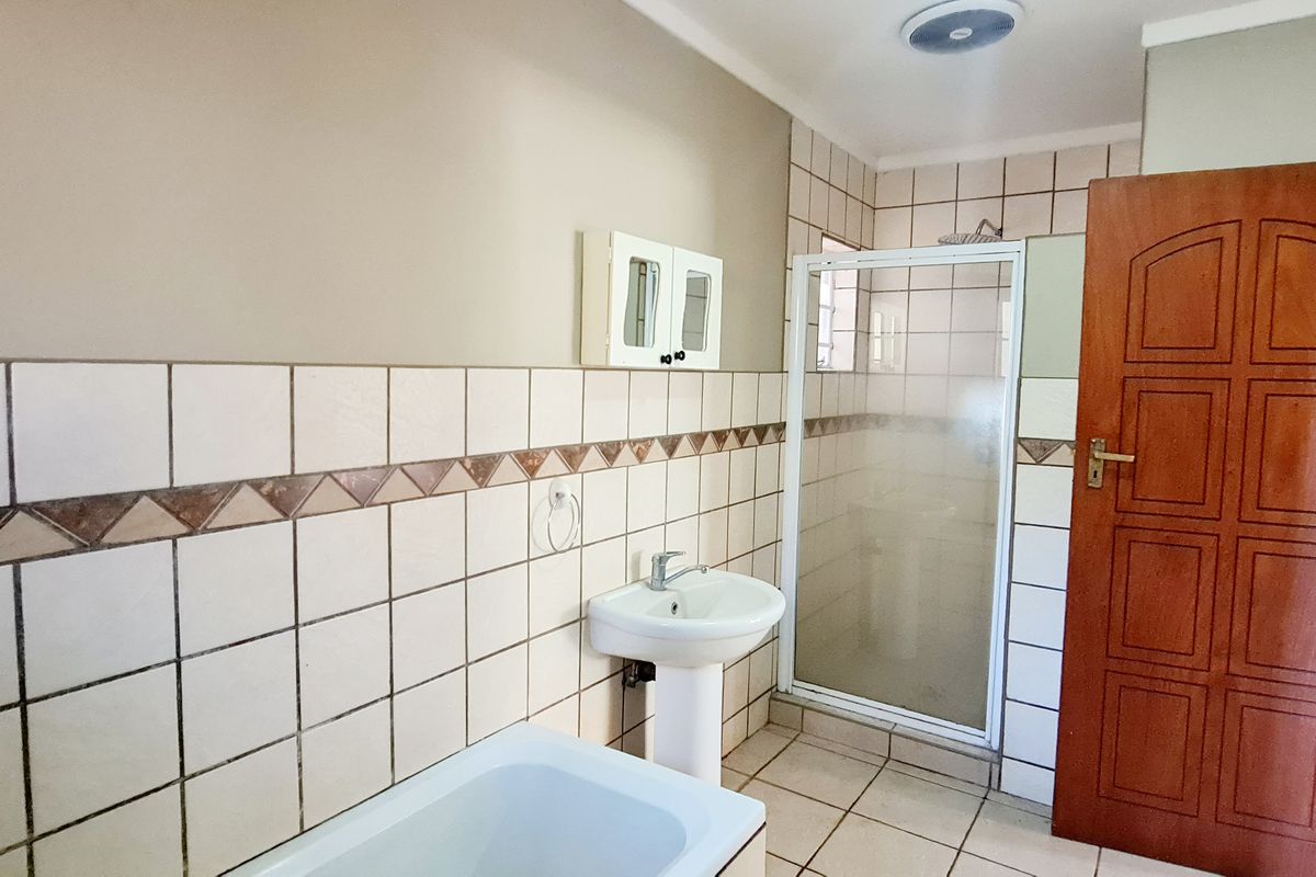 A functional bathroom featuring a pedestal basin, a separate shower enclosure, and a bathtub with neutral wall tiling.