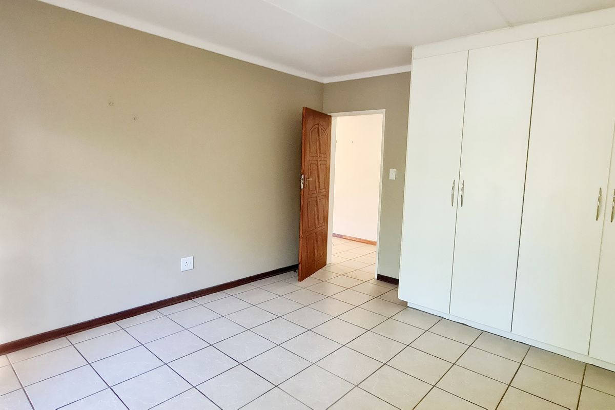 A bright, empty bedroom featuring neutral wall tones, tiled flooring, and ample built-in cupboard storage space.