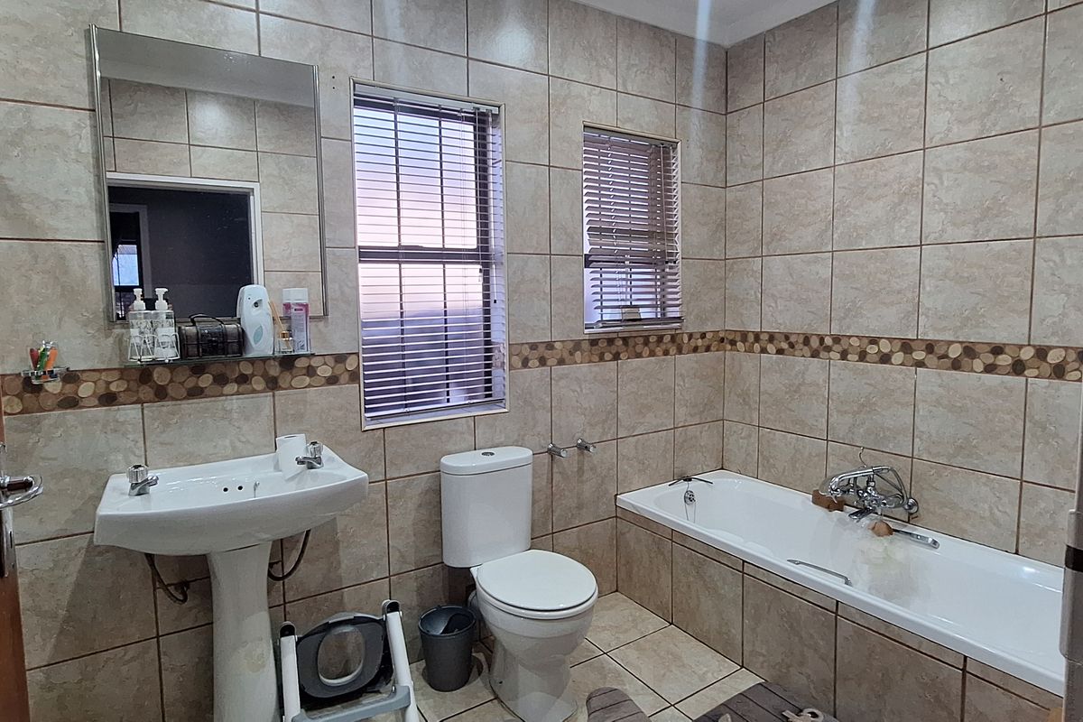 A functional bathroom featuring a pedestal basin, a standard bathtub, and full-height wall tiling with a decorative mosaic border.