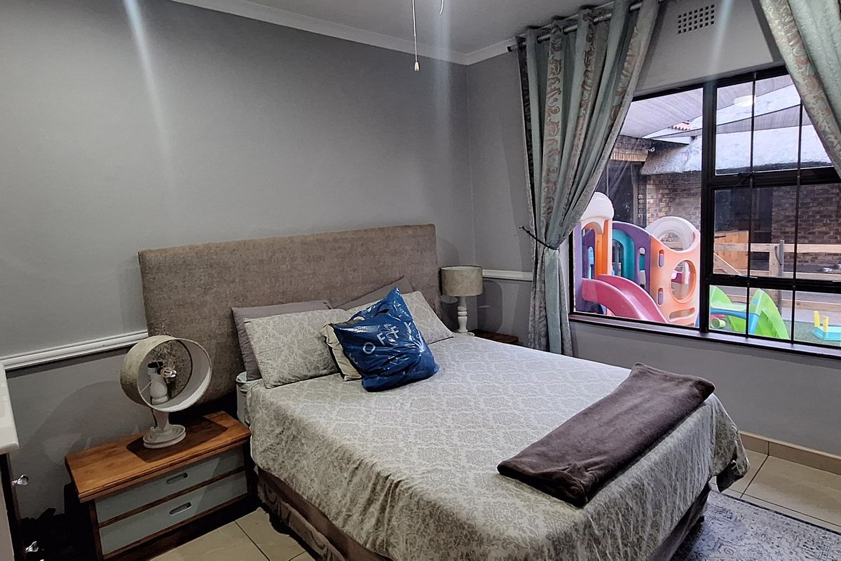 A well-lit bedroom featuring tiled flooring, a large window with curtains, and neutral wall finishes, providing a comfortable and functional living space.