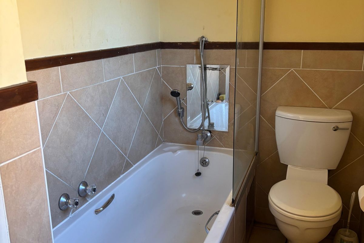 A functional bathroom featuring a bathtub with a glass shower screen, wall-mounted shower head, and a standard toilet.