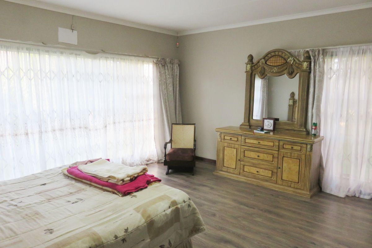 Spacious bedroom featuring wood-look laminate flooring, large windows with curtain treatments, and neutral wall finishes.
