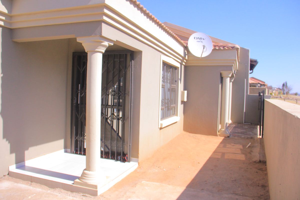 Rear exterior view featuring a tiled patio with decorative columns, security gates, and a boundary wall.