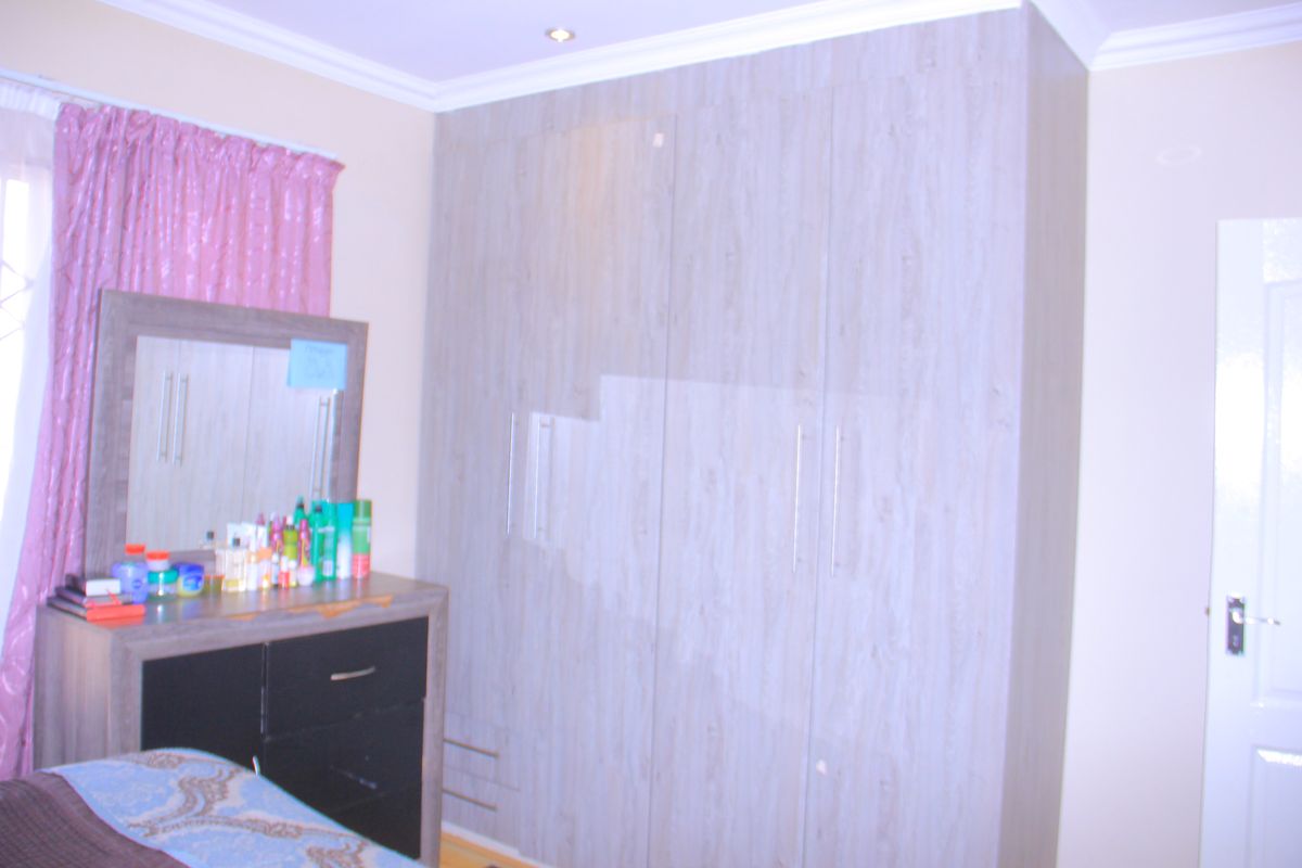 A bedroom featuring modern light wood-grain built-in cupboards, recessed ceiling lighting, and coved cornicing.