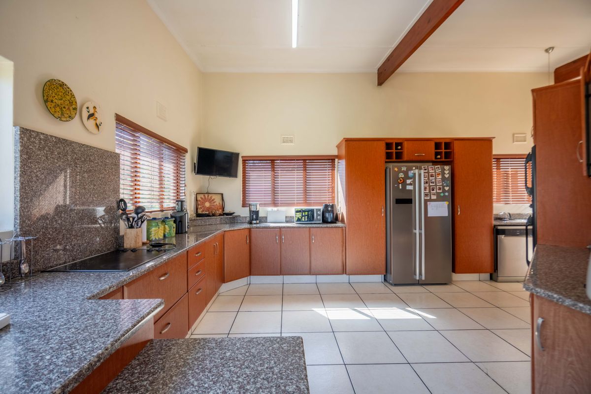 Spacious kitchen featuring granite countertops, extensive wooden cabinetry, ceramic tiled flooring, and an exposed timber ceiling beam, offering a functional and well-maintained workspace.