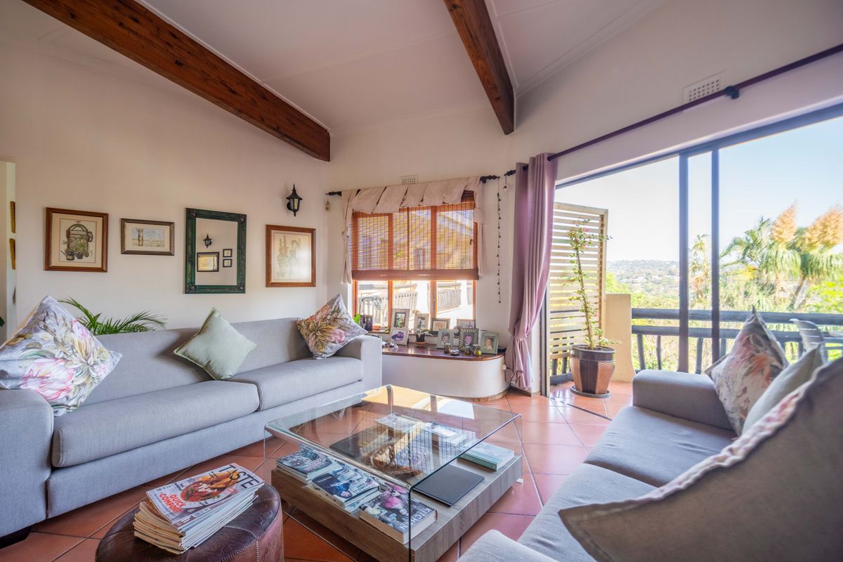 Spacious living room featuring exposed timber ceiling beams, terracotta flooring, and large sliding doors opening onto a balcony with scenic views.