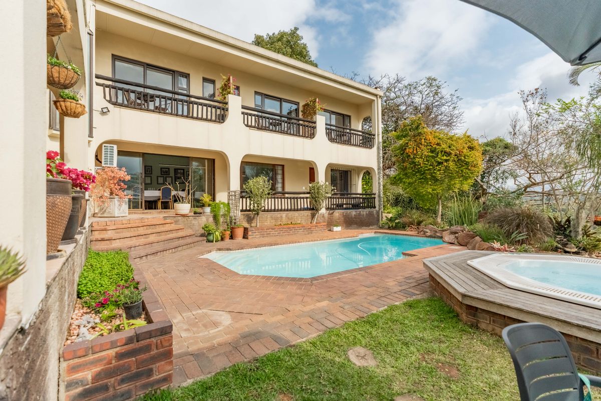 Rear exterior view featuring a swimming pool, built-in spa, brick paved patio area, and a two-story balcony overlooking the garden.